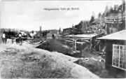 Facility with many buildings and piles of rocks and a rail line with a walkway leading above it