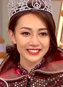 A close-up headshot of a young Asian woman smiling, wearing an ornate crown