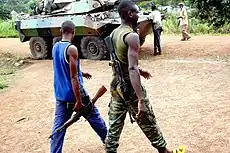 Two New Forces rebels walk by a French Foreign Legion AFV which stands in the background on a road