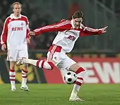 A white man, wearing the red and white football kit, kicking the ball.