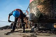 A sailor scrapes barnacles and other marine growth off of a buoy