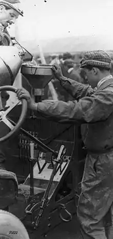 Two men pour water into their car's radiator using a funnel.