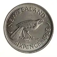 A silver-coloured New Zealand sixpence, 1965, featuring a Huia bird on a twig.