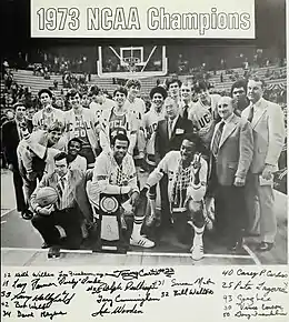 A black-and-white photograph of the 1972–73 UCLA Bruins men's basketball team posing with the NCAA championship trophy