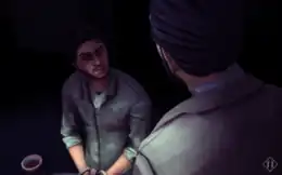 The player character is sitting, with his hands tied, and blood on his face and clothes. A dark-haired man looks down to him.