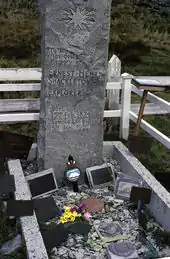 A tall stone column stands over a grave on which rest various memorabilia including a bunch of flowers. The stone is inscribed: "Ernest Henry Shackleton, Explorer, Born 15th February 1874. Died 5th January 1922".