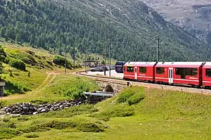 Red train approaching shelter located on bend in the railway line