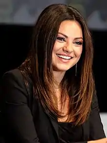 A woman with black hair, smiling while wearing a black dress.