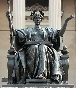 Bronze statue of a crowned woman sitting with an open book on her lap