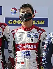 Photograph of Yifei Ye wearing a white uniform with red trim and a black medical mask on his face