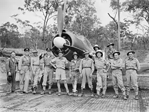 Twelve men wearing military uniforms standing in front of a single-engined World War II-era propeller fighter aircraft