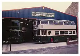 A double deck bus in front of a large iron clad garage