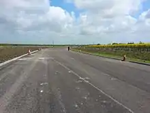 A picture of a paved, partly-complete A5758 road without any markings on its pavement and with traffic cones lining its sides