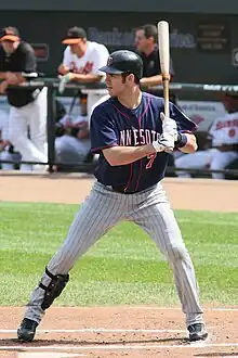 A man in a navy baseball jersey and batting helmet with gray pants