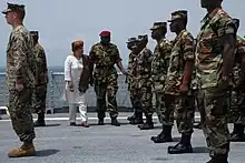 A colour photograph of soldiers on a naval vessel being inspected by President Ellen Johnson Sirlef and a senior military officer. The soldiers are wearing disruptive pattern camouflage uniforms and are standing in ranks across the deck