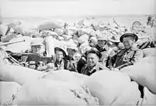 Soldiers wearing helmets sit in a sandbagged position near a machine gun