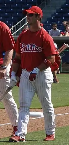 A man wearing a red baseball jersey and cap and white pinstriped baseball pants walking on a grass field