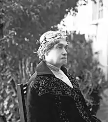 Black and white photograph of a woman sitting in profile wearing an embroidered jacket and a crown of laurels on her head.