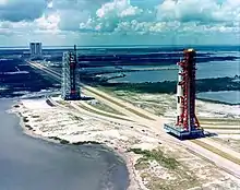 A tall rocket on a platform is rolled out along a track towards a launch site