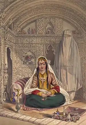 Picture of Shakar Lab, an Afghan lady. She is sitting crosslegged on the ground with a large cushion behind her. She is wearing green skirts, a yellow shirt, a white veil hanging behind her, and jewelry. In her hands is a pink rose, and her long black hair falls freely. Behind her is an alcove covered in carvings of foliage. In front of her is a water-pipe and a box of small pots; behind and to the right is a standing woman in a burqa, face covered.