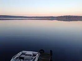 A very calm lake at sunset, showing trees on the far shore