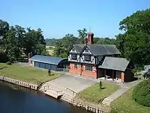 An elevated view of a house with a brick lower storey and the upper storey half-timbered, with the river running across its front