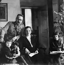 A man, a woman, and a child are on the left, posed to face the camera. To the right is a girl, drawing