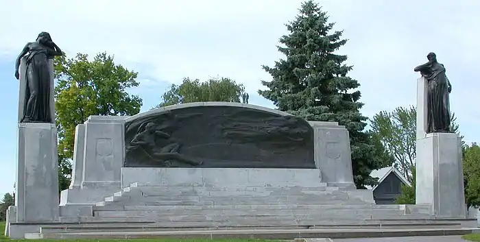 A majestic, broad monument with figures mounted on pedestals to its left and right sides. Along the main portion of the monument are five figures mounted on a broad casting, including a man reclining, plus four floating female figures representing Inspiration, Knowledge, Joy, and Sorrow.