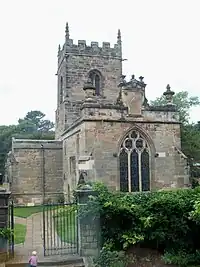 A stone church seen from the east.  It has a three-light east window, over which is a sundial, and beyond it is a battlemented tower