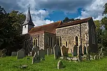 A flint church with a red tied roof and a tower at the west end, seen from the southeast