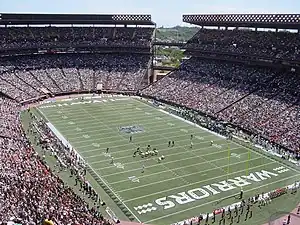 A football field with players lined up in the middle of it surrounded by a packed stadium