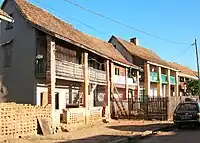 Two-story brick house with peaked roof and simple second-floor covered veranda supported by four equidistant pillars