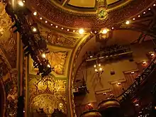 A side view of the balcony-level seats, looking up from the orchestra level. There are murals on the walls.