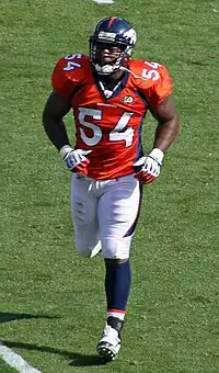 Andra Davis, a six-foot-one African-American man, jogs to the football sideline in the orange, white and navy uniform of the Denver Broncos, circa 2009.