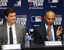 Andrew Miller and Mariano Rivera sit at a table at a press conference dressed in suits.