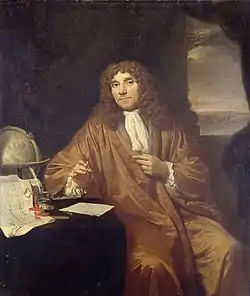 painting of Antonie van Leeuwenhoek, in robe and frilled shirt, with ink pen and paper