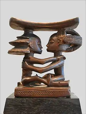 Headrest; 19th century; wood; height: 18.5 cm (7.2 in), width: 19 cm (7.4 in), thickness: 8 cm (3.1 in); Musée du quai Branly (Paris). This headrest presents 19th century Luba hairstyles, as well as the long limbs, bent-back legs, cylindrical torso and dynamic pose typical of the artist who made it