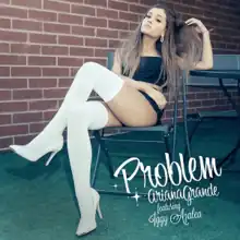 A picture of a woman sitting down in a chair wearing white thigh high socks, crop top and shot. Behind her there is a brown brick wall and to the side of her are the words "Problem Ariana Grande featuring Iggy Azalea" in white chalk writing. Her right hand is touching her long brunette-hair.