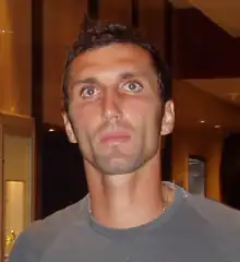 A upper-body photograph of a brown-haired, brown-eyed white man wearing a grey shirt.