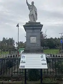 Photograph of a statue depicting Fr Michael Murphy atop a plinth, with his arm raised. The plinth bears the year "1798", and a portrait of Wolfe Tone.