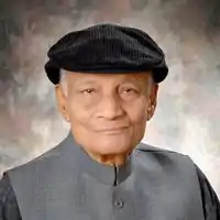 Colour photo headshot of Asad Muhammad Khan wearing a black flatcap