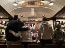 Image of the interior of Hughes Auditorium. Shows people arm in arm in front of a large organ.