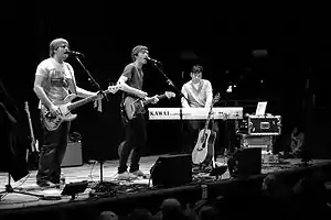 Several men performing onstage playing instruments and singing into a microphone