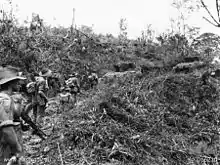 Men armed with rifles and light machine-guns advance along a track behind an armoured vehicle