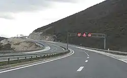 Variable traffic signs placed on a gantry indicating speed limit for each traffic lane and slippery road surface warning.