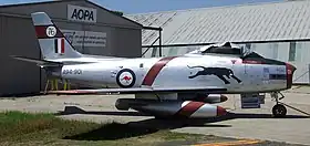 Sabre single-engined jet fighter painted silver and parked in front of a hangar