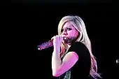 Avril Lavigne wearing a black gown and singing in to a microphone.