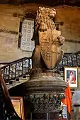 A lion puissant holding the coat of arms of Bombay. In the backdrop is a portrait of the Hon. Jugonnath Sunkersett, one of the founding fathers of the city of Mumbai.