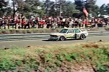 Photograph of the racing car driving on the tracks with spectators in the background