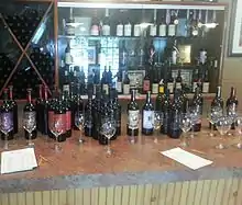 Rows of wine glasses and wine bottles on a bar, with a glass cabinet in the background displaying awards.